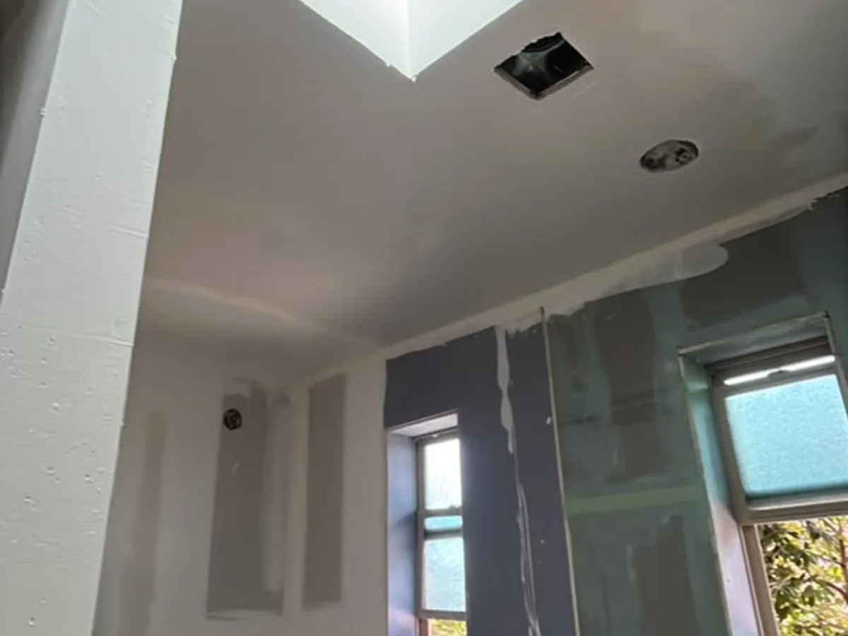 Hallway ceiling repair beside a skylight with finished drywall on the wall